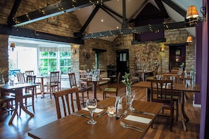 A restaurant with wooden tables and chairs, stone walls, and string lights. - Corinium Hotel & Restaurant (Cirencester)