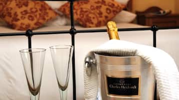 Uma cama com estrutura metálica, dois flûtes de champanhe, uma garrafa de champanhe Charles Heidsieck e um prato com morangos sobre uma mesa de madeira.