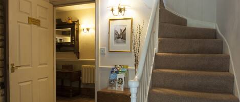 A staircase with carpeted steps, a white handrail, and a small table with a sign and a vase of branches.