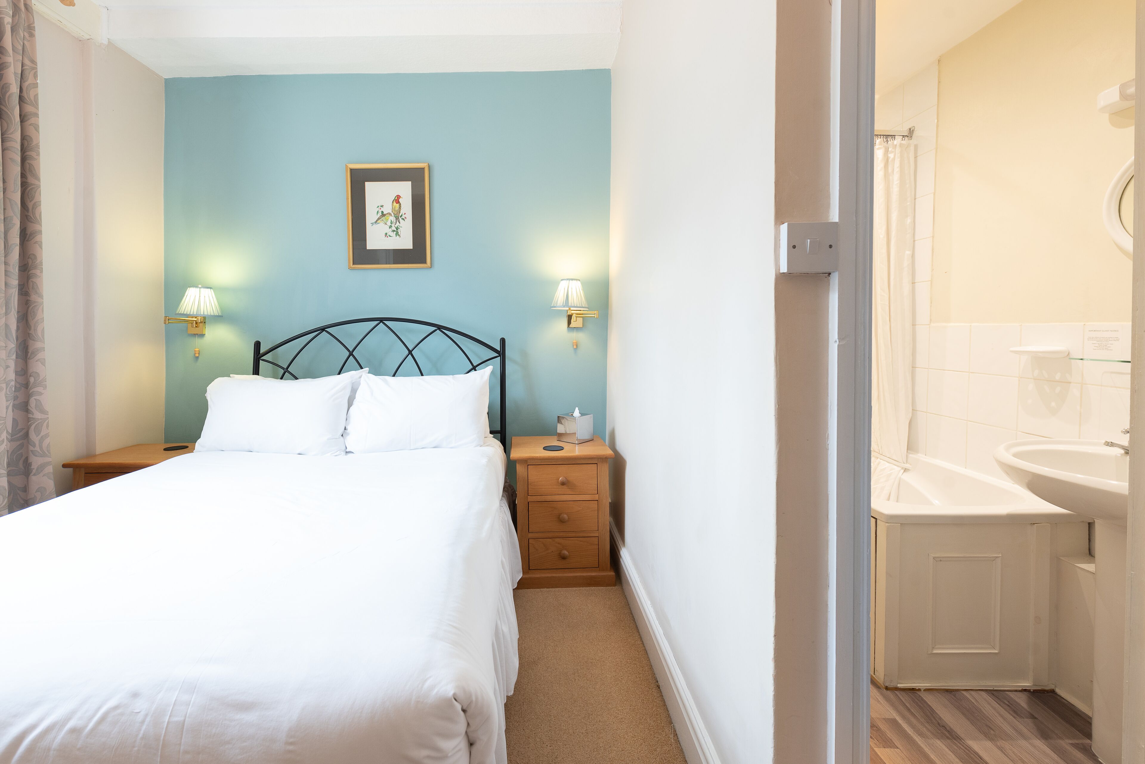 A neatly made bed with white linens, a wooden nightstand with two wall-mounted lamps, and a framed picture on the wall.