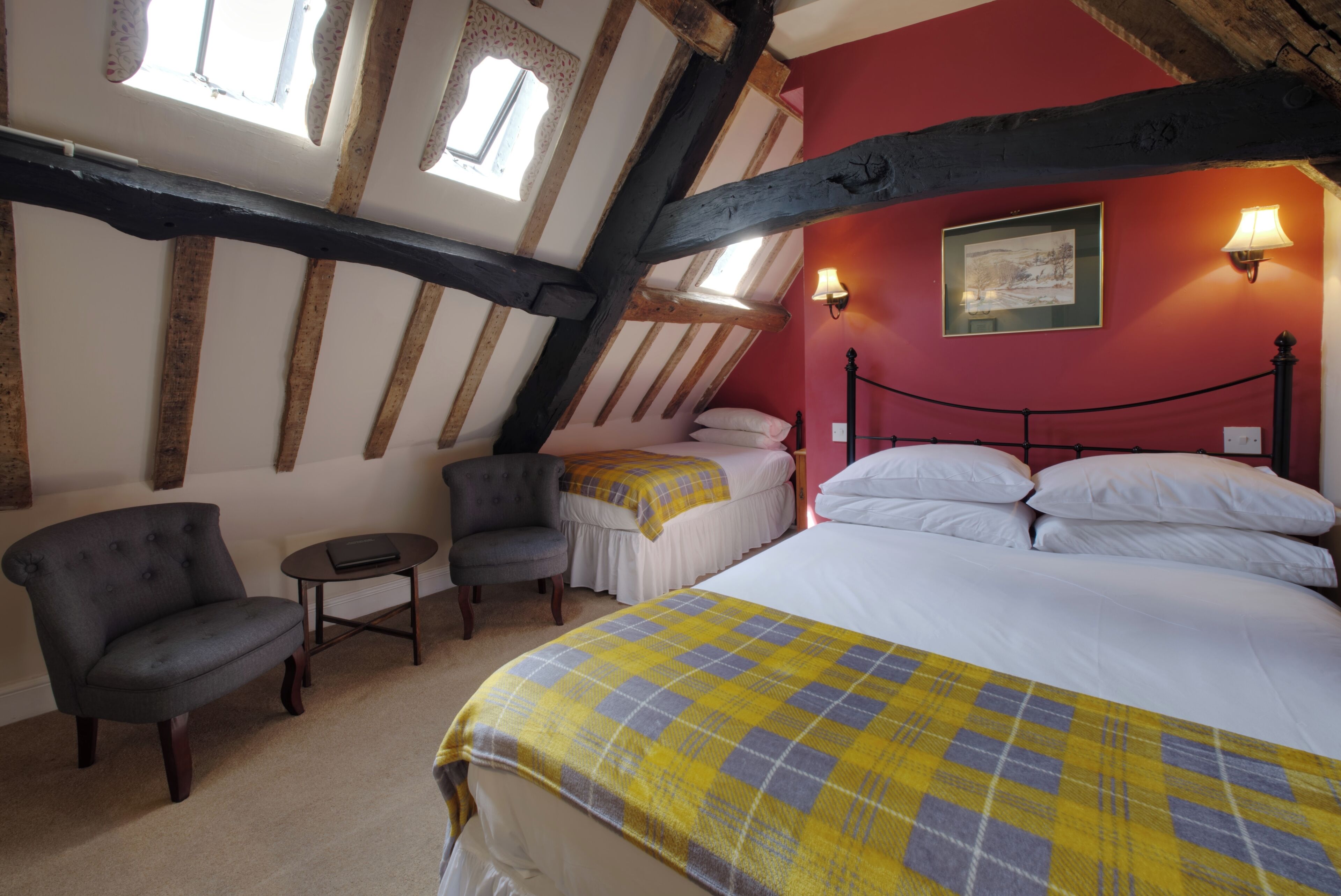 A bedroom with a bed, two chairs, a small table, and a window.