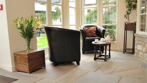Una habitación amplia con un ventanal grande, un sillón de cuero negro, una mesita con un hervidor de agua y una alfombra estampada.