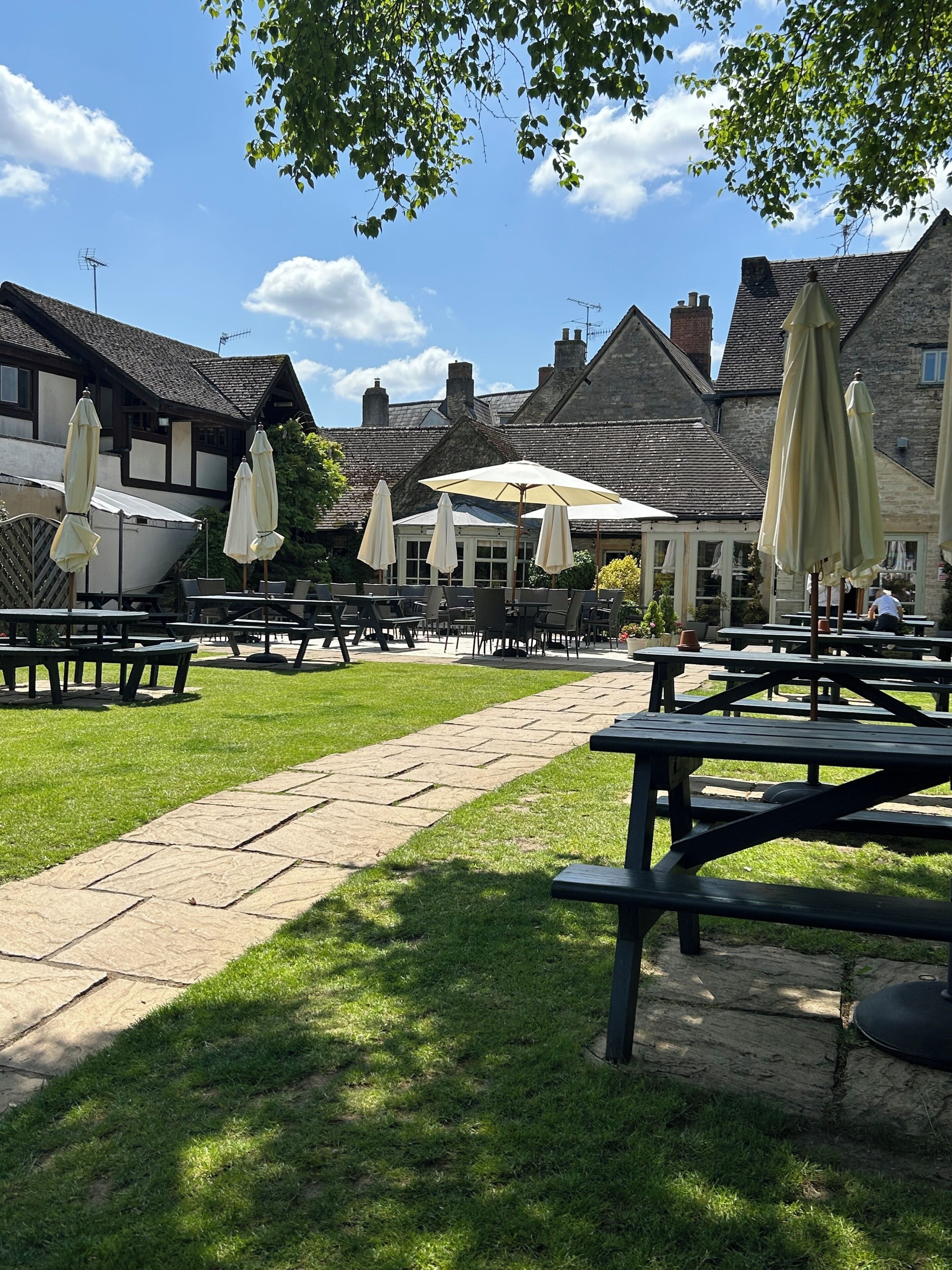 An outdoor seating area with picnic tables and umbrellas, surrounded by stone buildings with traditional architecture.