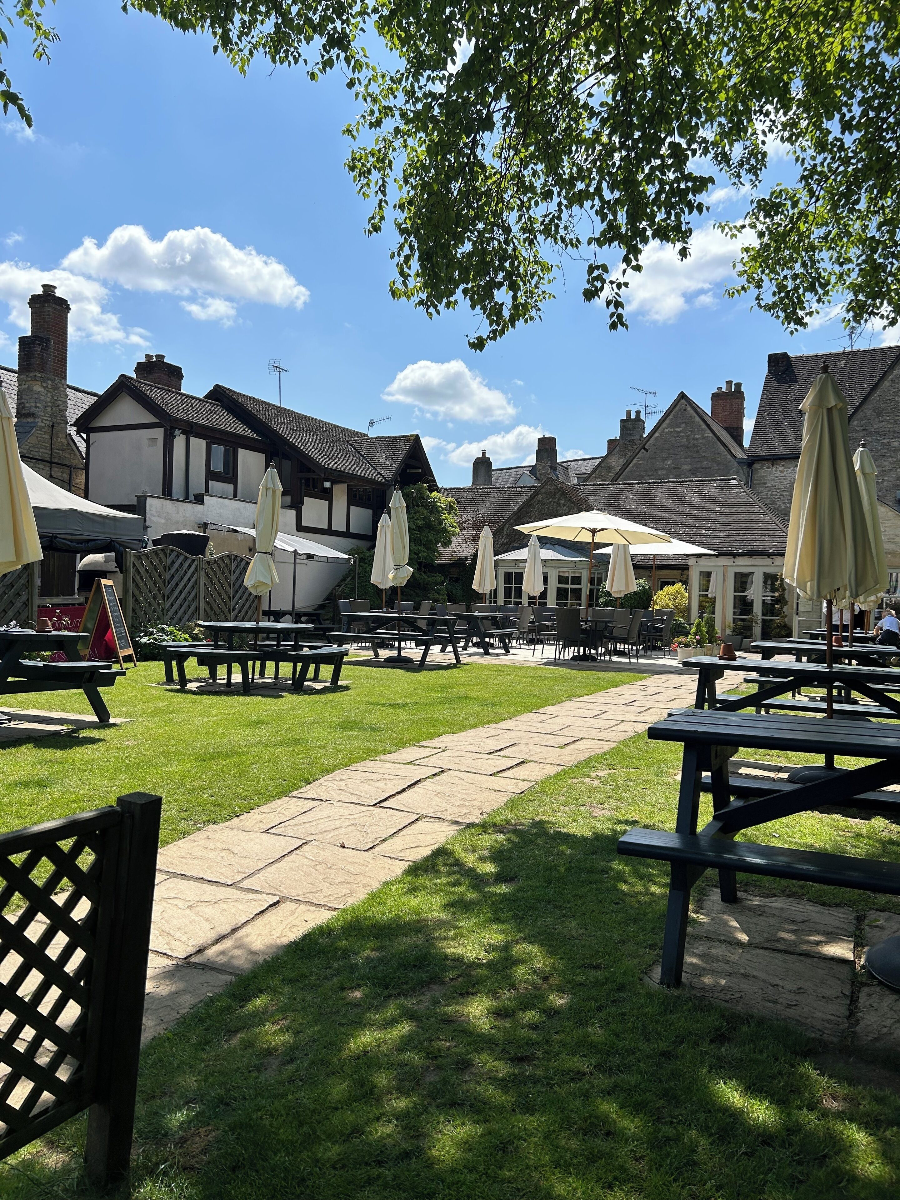 An outdoor seating area with picnic tables and umbrellas, surrounded by buildings with stone chimneys and traditional architecture.