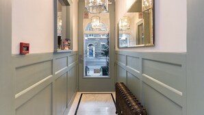 A hallway with a door leading to a street view, a fire alarm, a bench, and a mirror on the wall. - Staunton Hotel (London)
