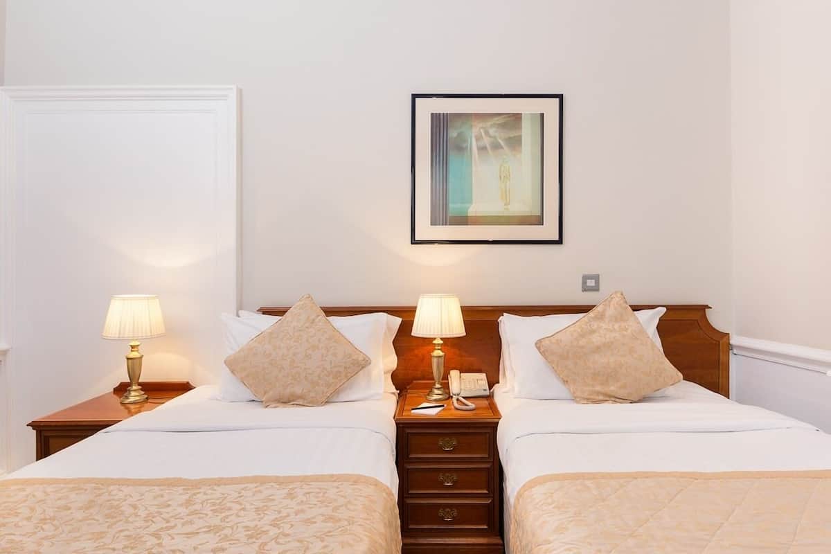 A hotel room with two beds, a nightstand with a lamp, a framed picture on the wall, and a wooden headboard.