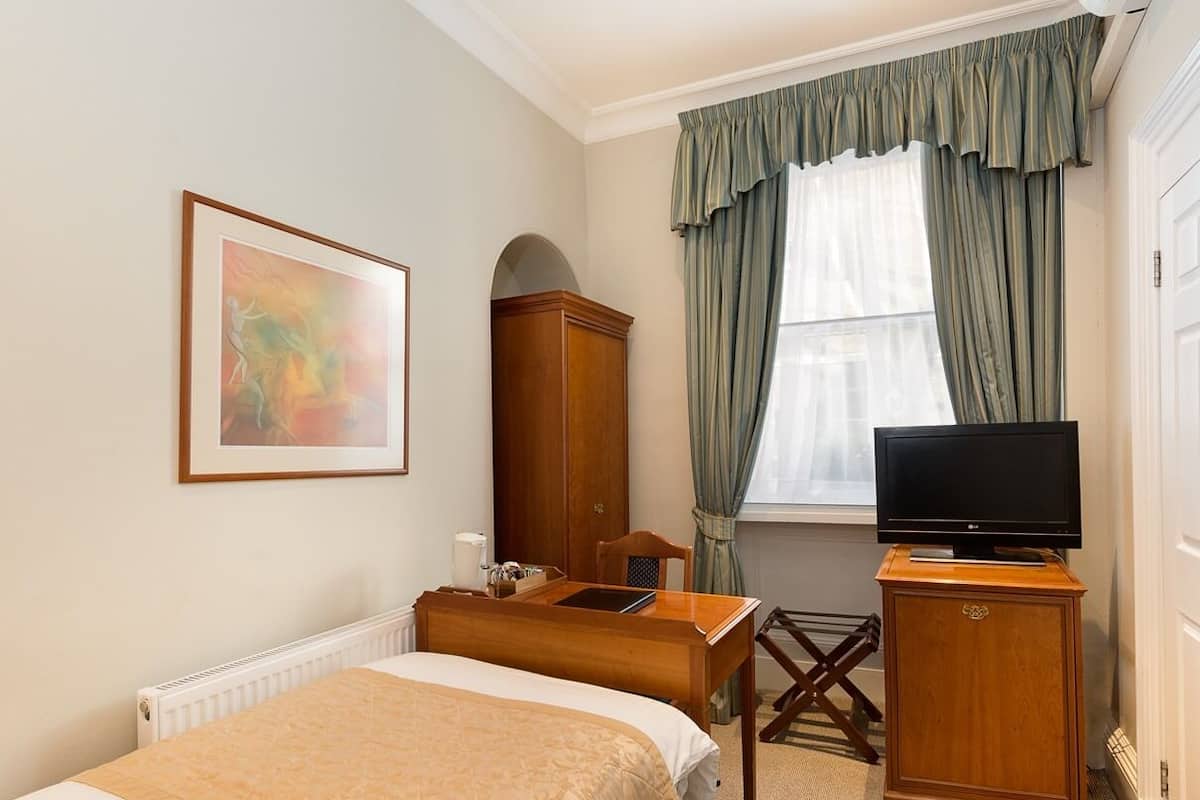 A hotel room with a bed, a desk, a television, a wardrobe, and a window with curtains.