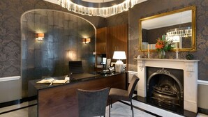A modern interior with a dark wood reception desk, a fireplace, and a large mirror above it. - Staunton Hotel (London)