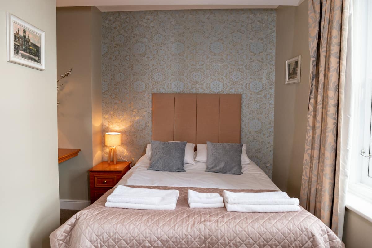 A neatly made bed with a quilted headboard, a bedside lamp, and a set of towels.