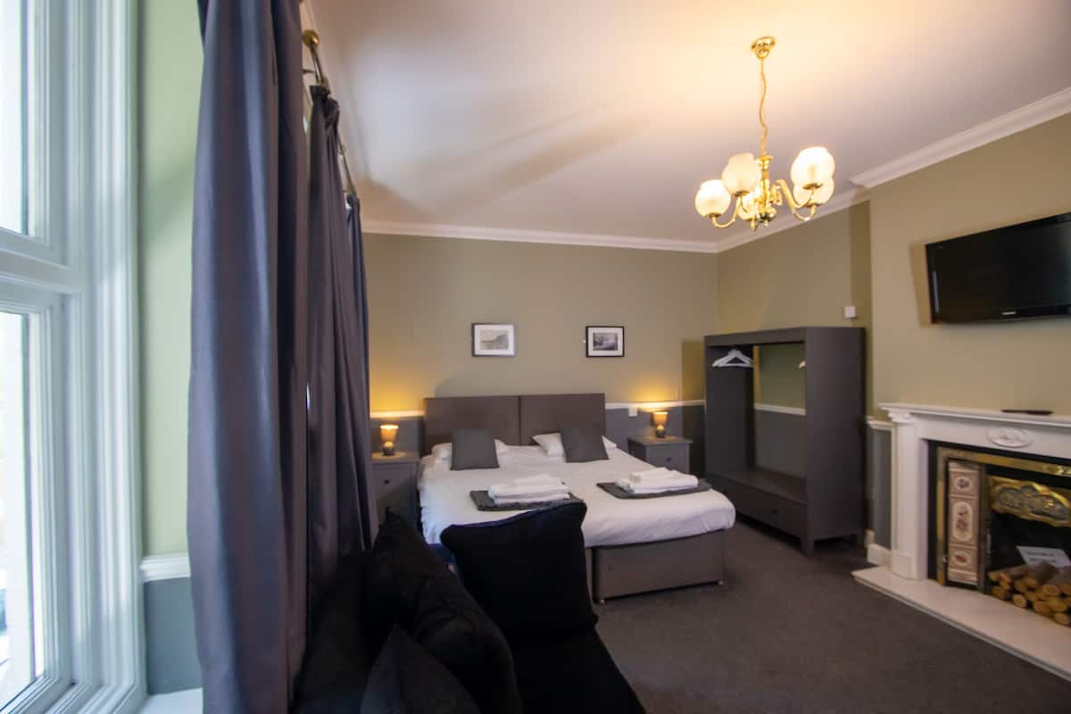 A hotel room with a bed, a desk, a television, and a fireplace.