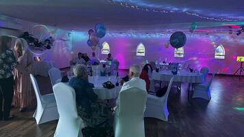 Une salle avec des tables et des chaises rondes, décorée de ballons et de guirlandes lumineuses.