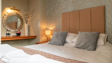 A hotel room with a large bed, a bedside table with a mirror, a lamp, and a decorative vase with branches.