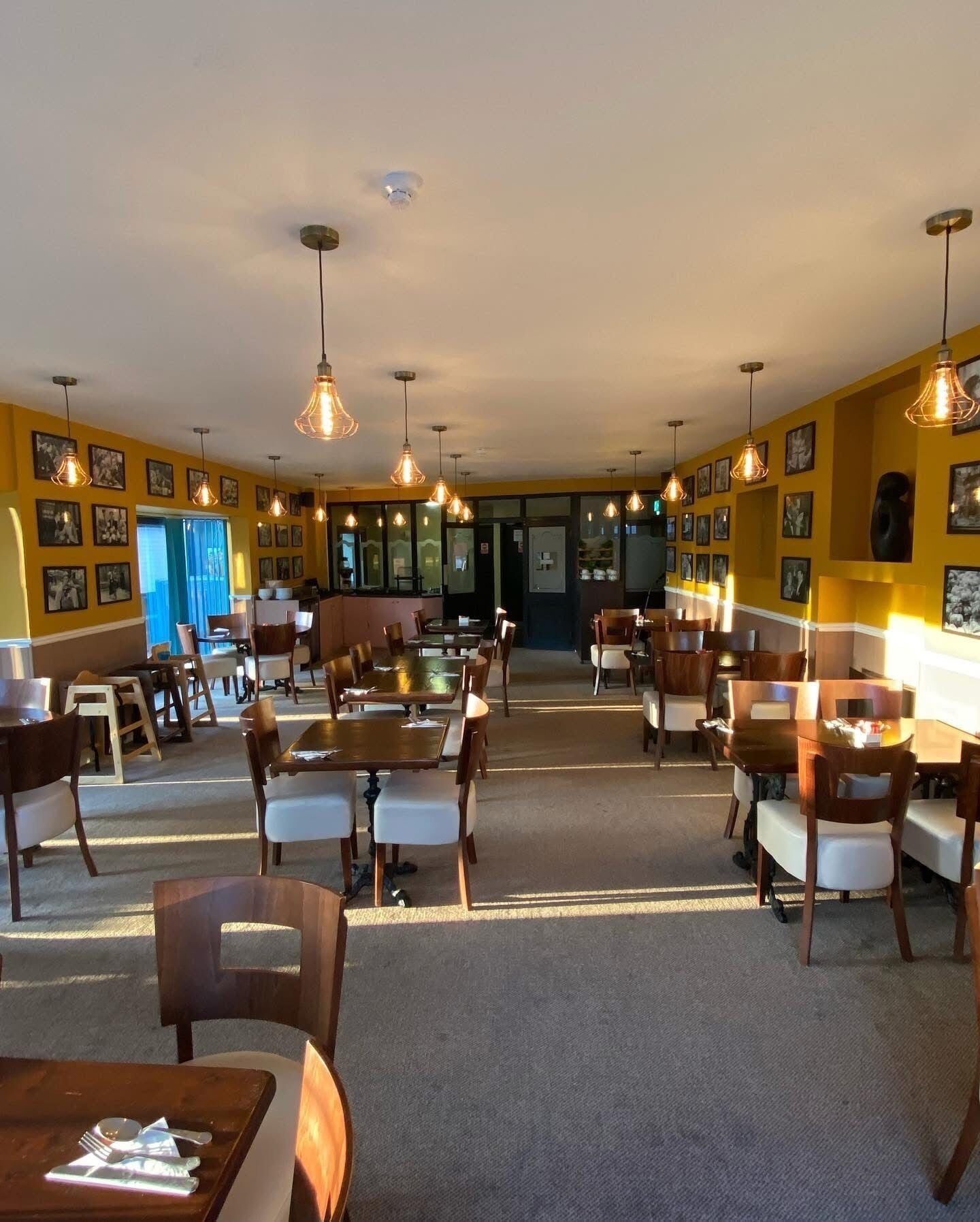 En rymlig restaurang med högt i tak, hängande lampor och ett stort, öppet område i mitten. Bord och stolar är placerade ut för att skapa en trevlig matplats.