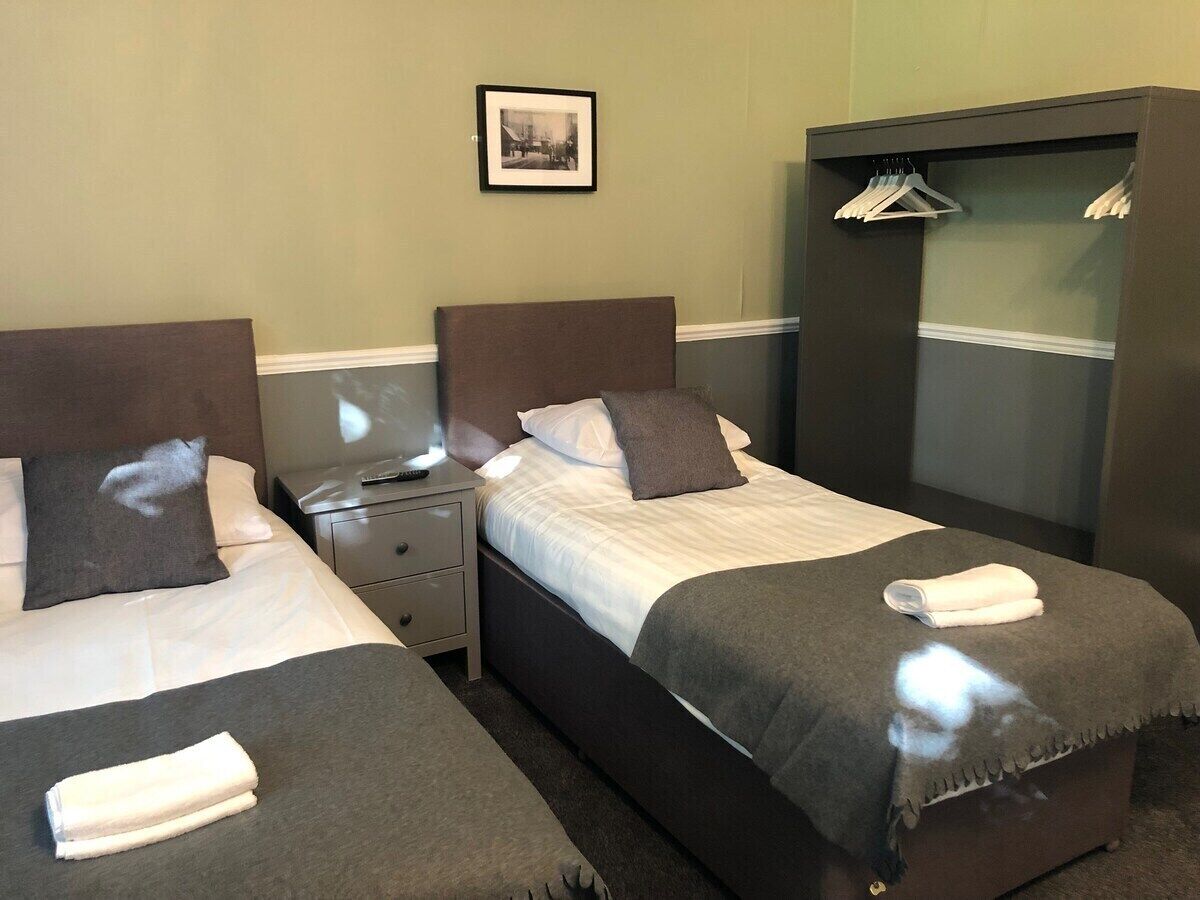 Habitación de hotel con dos camas, una mesita de noche, un armario y un cuadro en la pared.