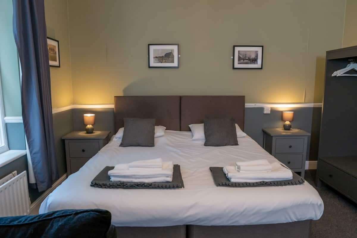 A hotel room with a large bed, two bedside tables with lamps, and two framed pictures on the wall.
