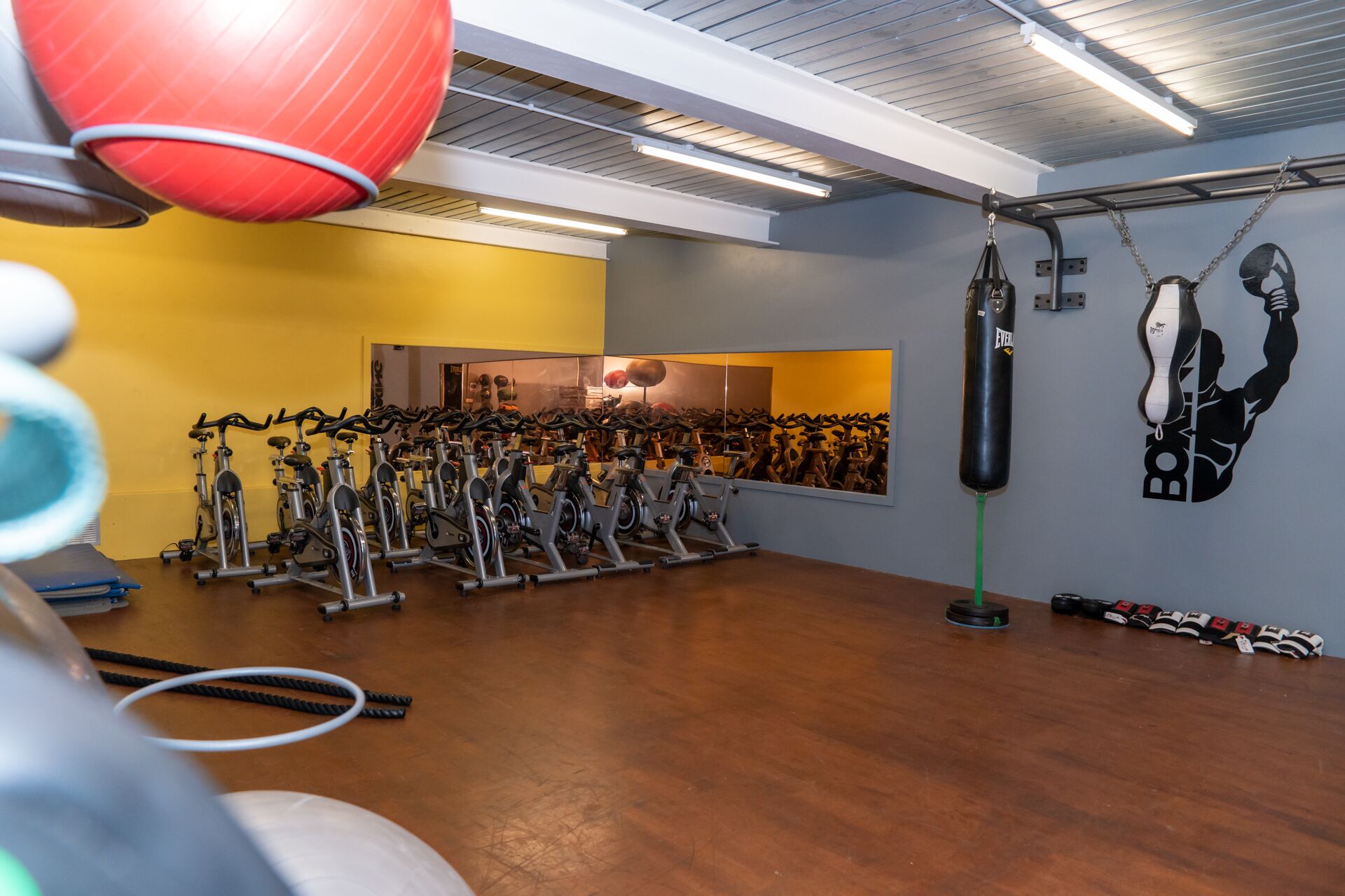 Een sportschool met meerdere trainingsfietsen, een bokszak en een spiegel die de fietsen weerspiegelt.