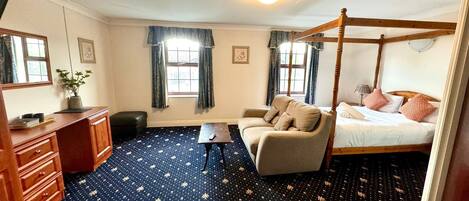 A bedroom with a four-poster bed, a sofa, a desk, and a chair.