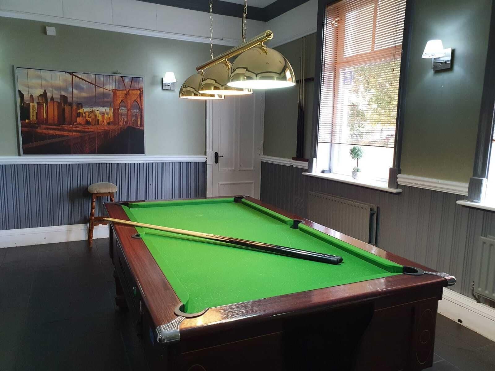 A pool table with a green felt surface, a pool cue, and a wooden chair.