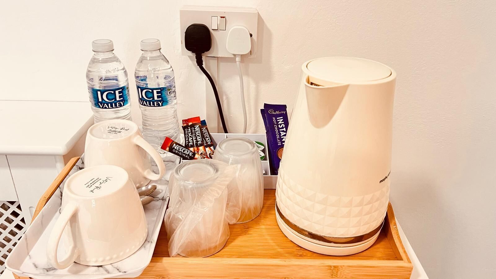 Een dienblad met een koffiezetapparaat, twee waterflessen, een koffiemok, een glas, een pakje Nescafé oploskoffie en een Cadbury chocoladereep.