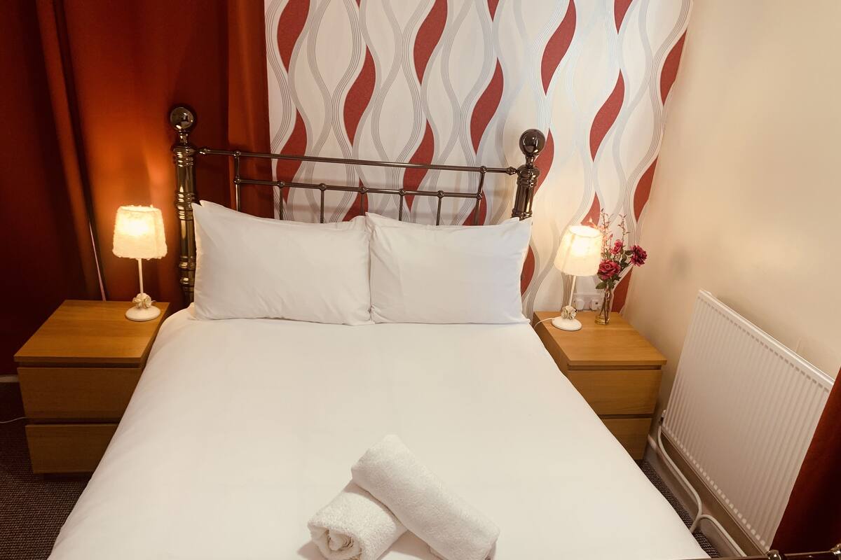 A neatly made bed with white linens, two bedside lamps, and a rolled white towel on the bed.