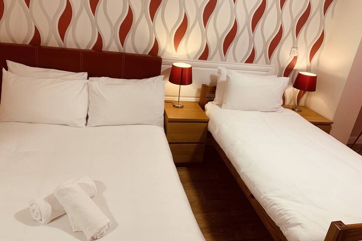 A hotel room with two single beds, a wooden headboard, a patterned wallpaper, and two bedside lamps.