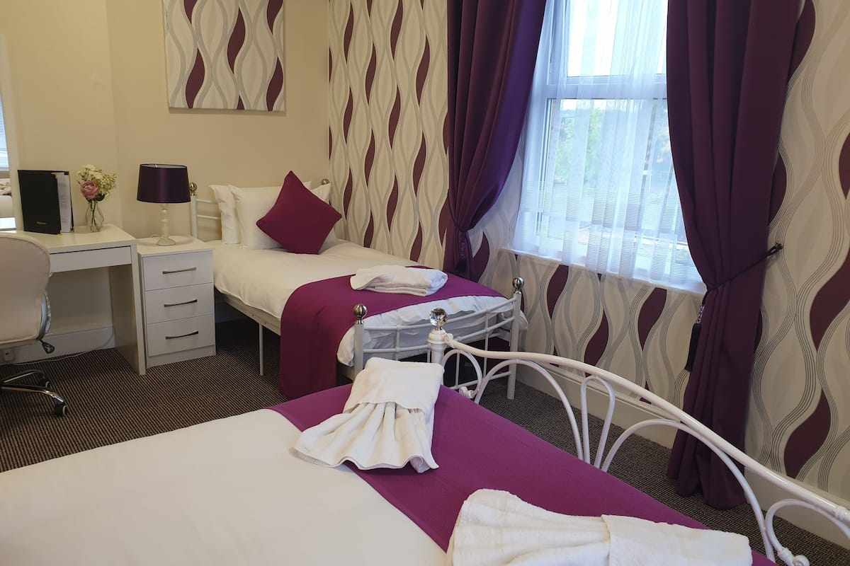 A hotel room with a bed, a desk, a chair, and a window with curtains.