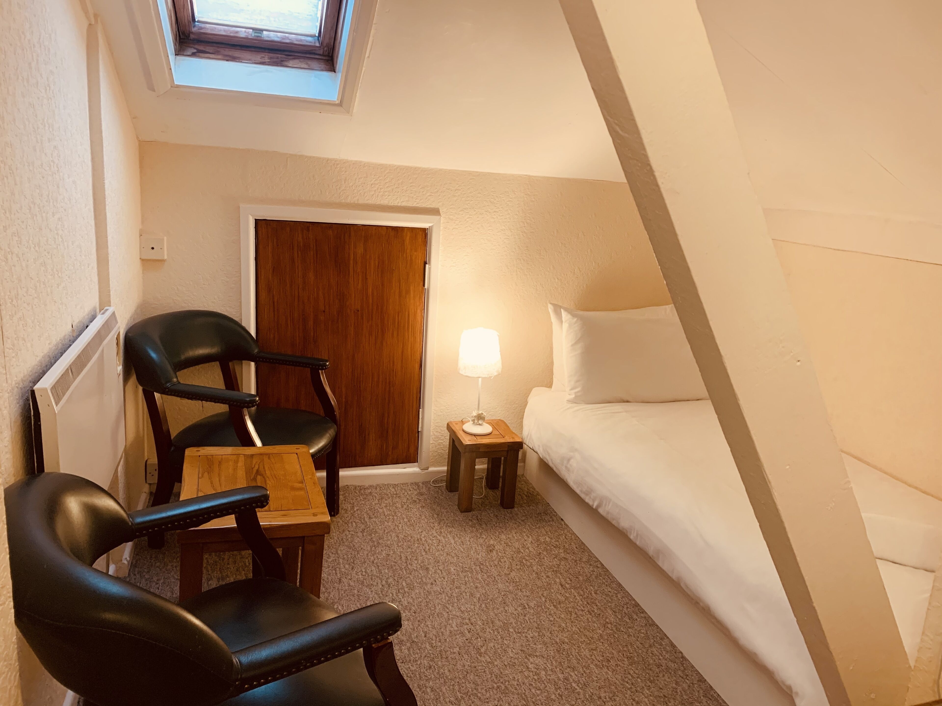 A small, cozy room with a bed, a chair, a table, and a lamp.