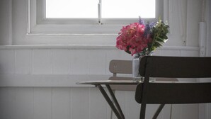 Une pièce avec une fenêtre, une table ornée d’un vase de fleurs et un banc.