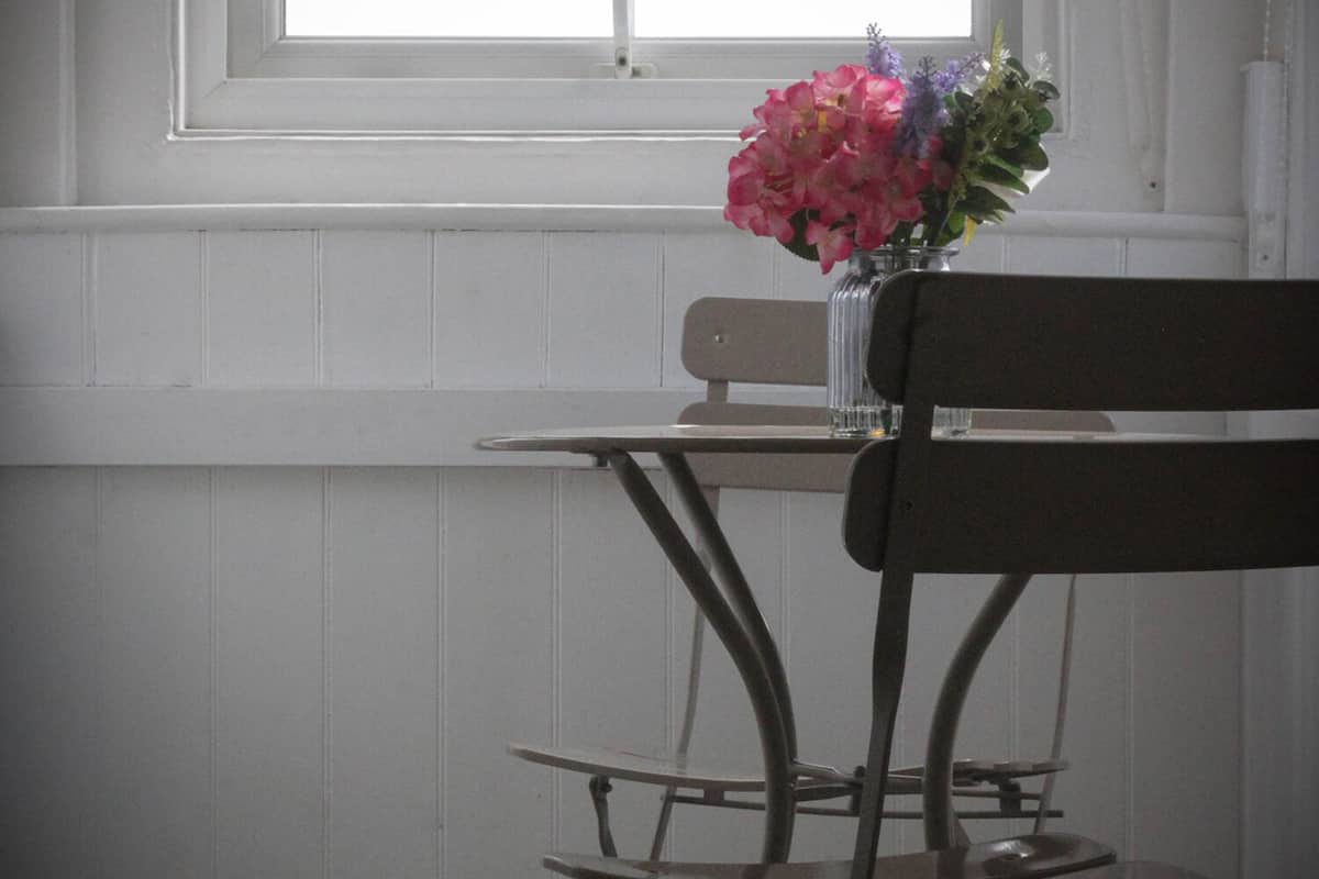 A room with a window, a table with a vase of flowers, and a bench.
