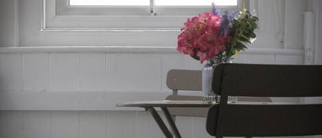 A room with a window, a table with a vase of flowers, and a bench.