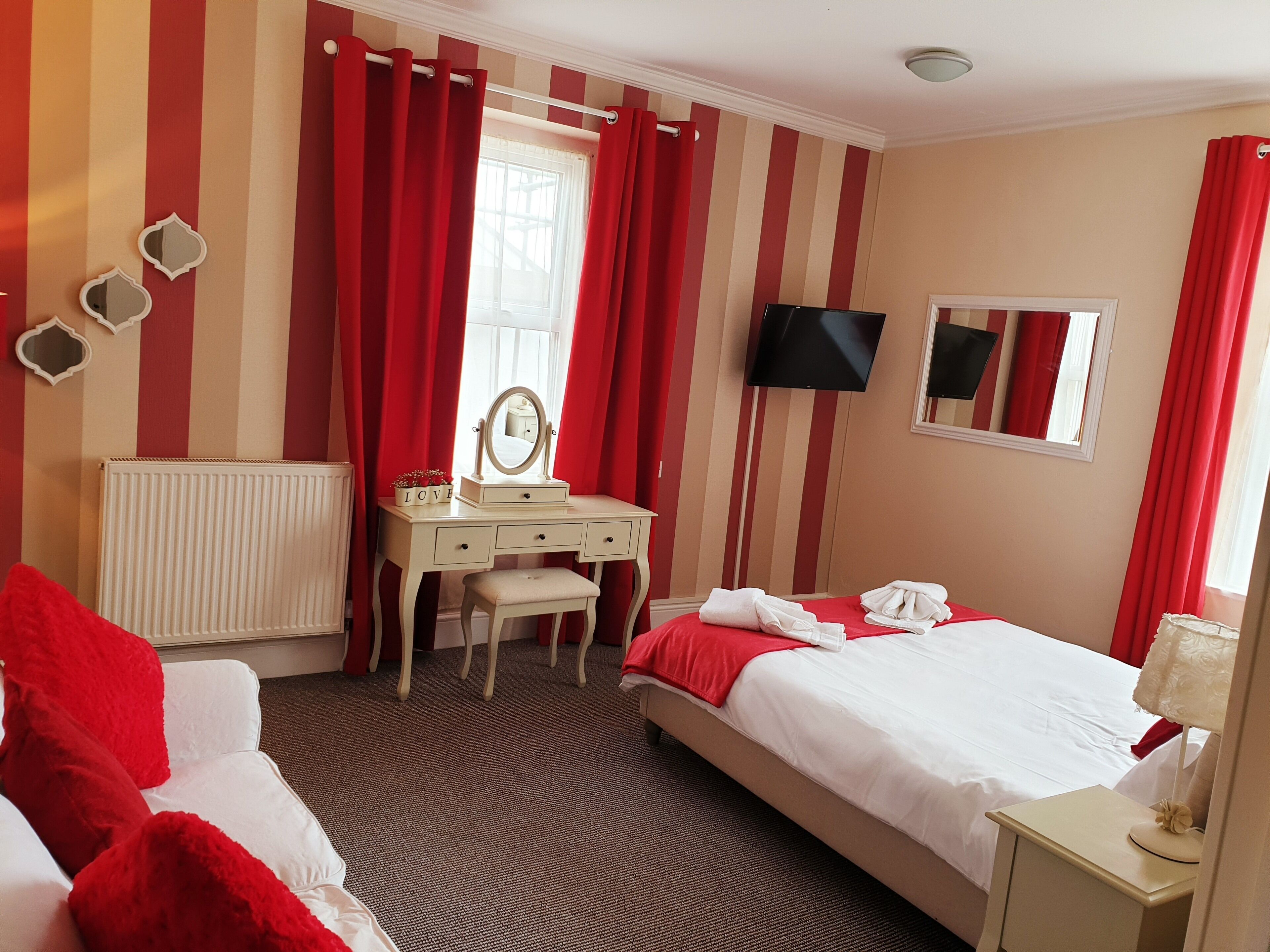 Habitación de hotel con cama, escritorio con espejo, radiador y televisor en la pared.