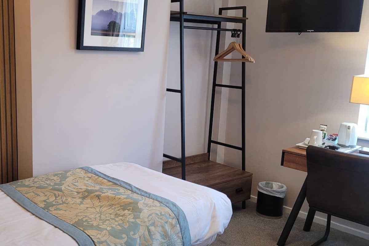 Ein Hotelzimmer mit Bett, Schreibtisch, Stuhl, Fernseher und einem Bild an der Wand.