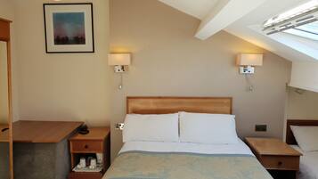 A hotel room with a bed, bedside tables, a desk, a lamp, a picture on the wall, and a skylight.