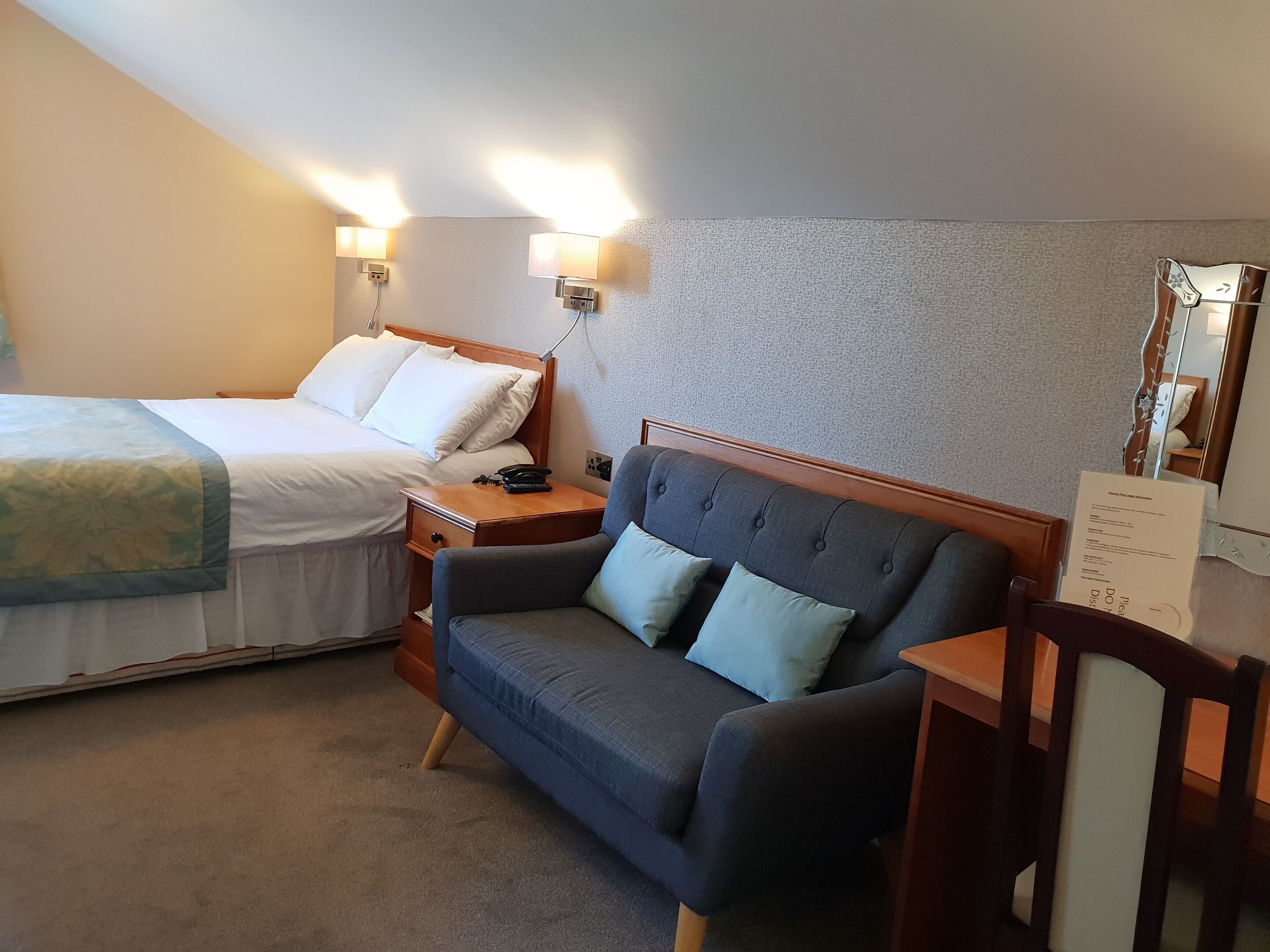 Una habitación de hotel con cama, sofá, mesita de noche y lámpara de pared.