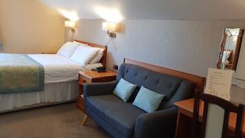 Una habitación de hotel con cama, sofá, mesita de noche y lámpara de pared.