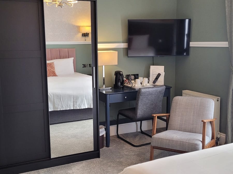 A hotel room with a bed, a desk with a chair, a TV, and a window with curtains.