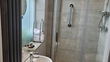 Een moderne badkamer met een douchecabine van glas, een witte wastafel en een handdoekhouder.