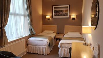A hotel room with two beds, a desk, a chair, a radiator, and a picture on the wall.
