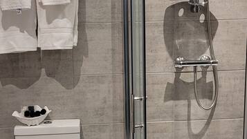 A modern bathroom with a glass-enclosed shower, a toilet, and a towel rack.