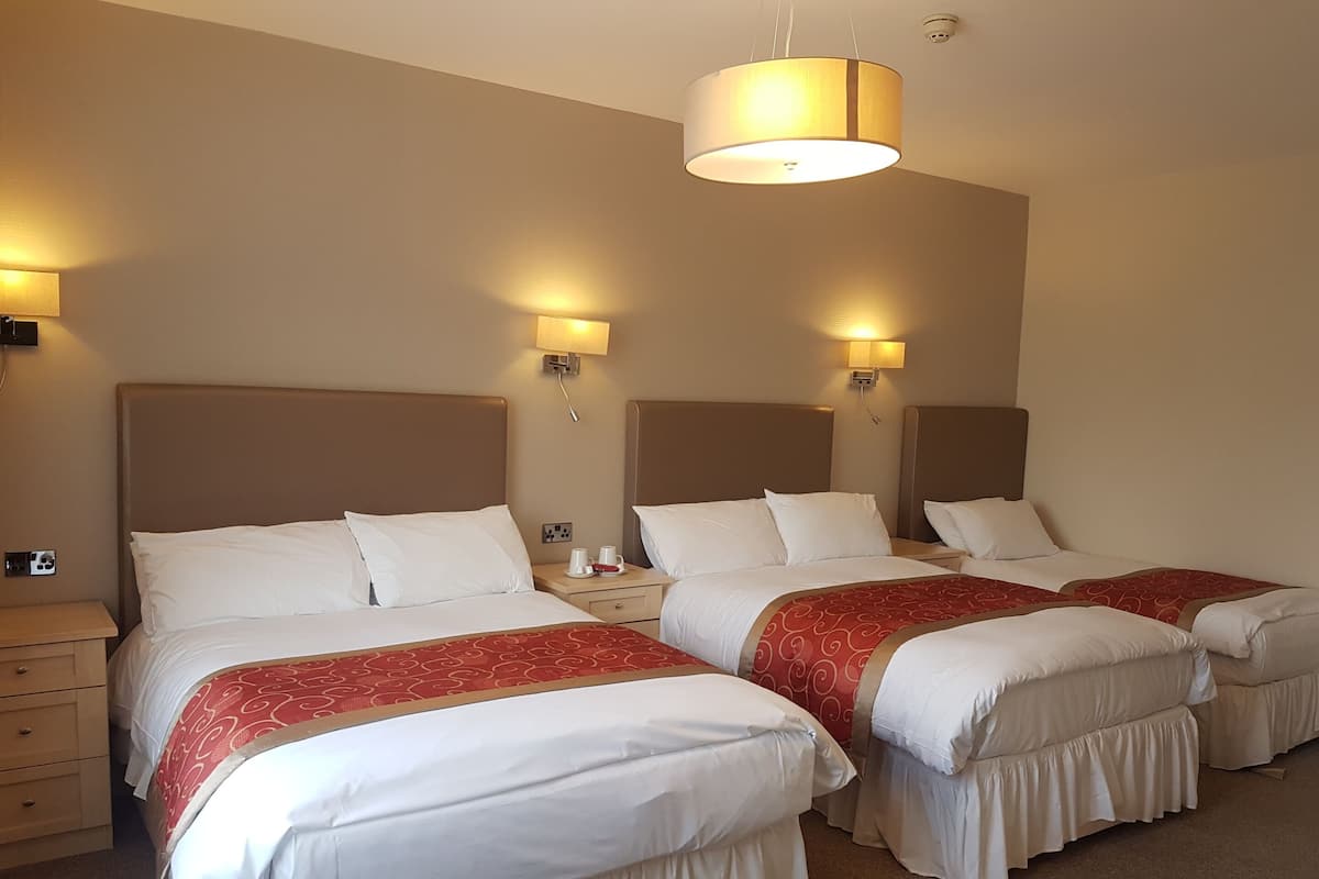 Ein Hotelzimmer mit drei Betten, jeweils mit weißer Bettwäsche und roten Akzenten, einer großen Deckenleuchte sowie Wandlampen.