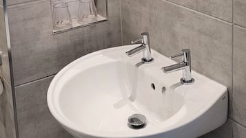 A bathroom with a white sink, two faucets, a mirror, and a towel dispenser.
