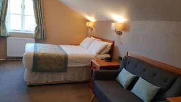 A hotel room with a bed, bedside table, lamp, and a sofa.