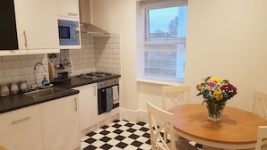 A kitchen with white cabinets, a black and white checkered floor, a microwave, a stove, and a dining table with chairs. - Gateway Hotel (London)