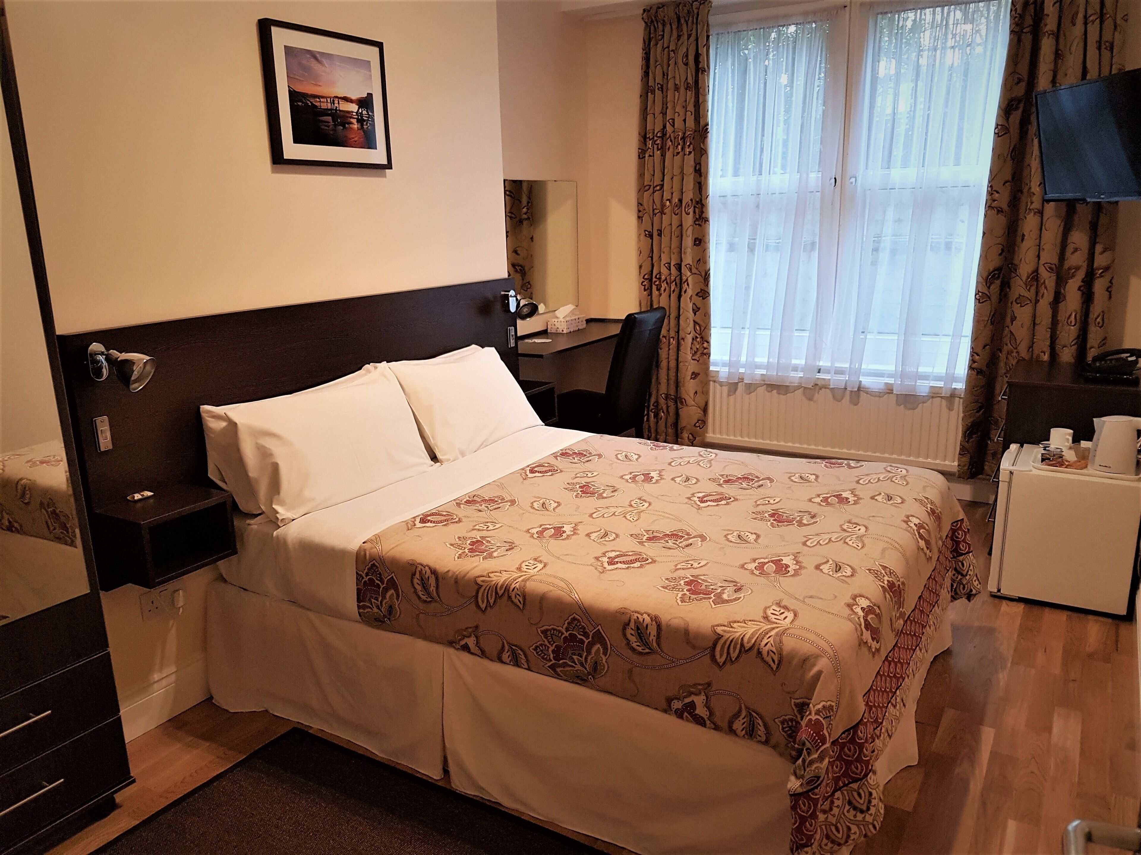 A hotel room with a bed, a desk, a chair, a TV, and a window with curtains.