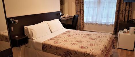 A hotel room with a bed, a desk, a chair, a TV, and a window with curtains.