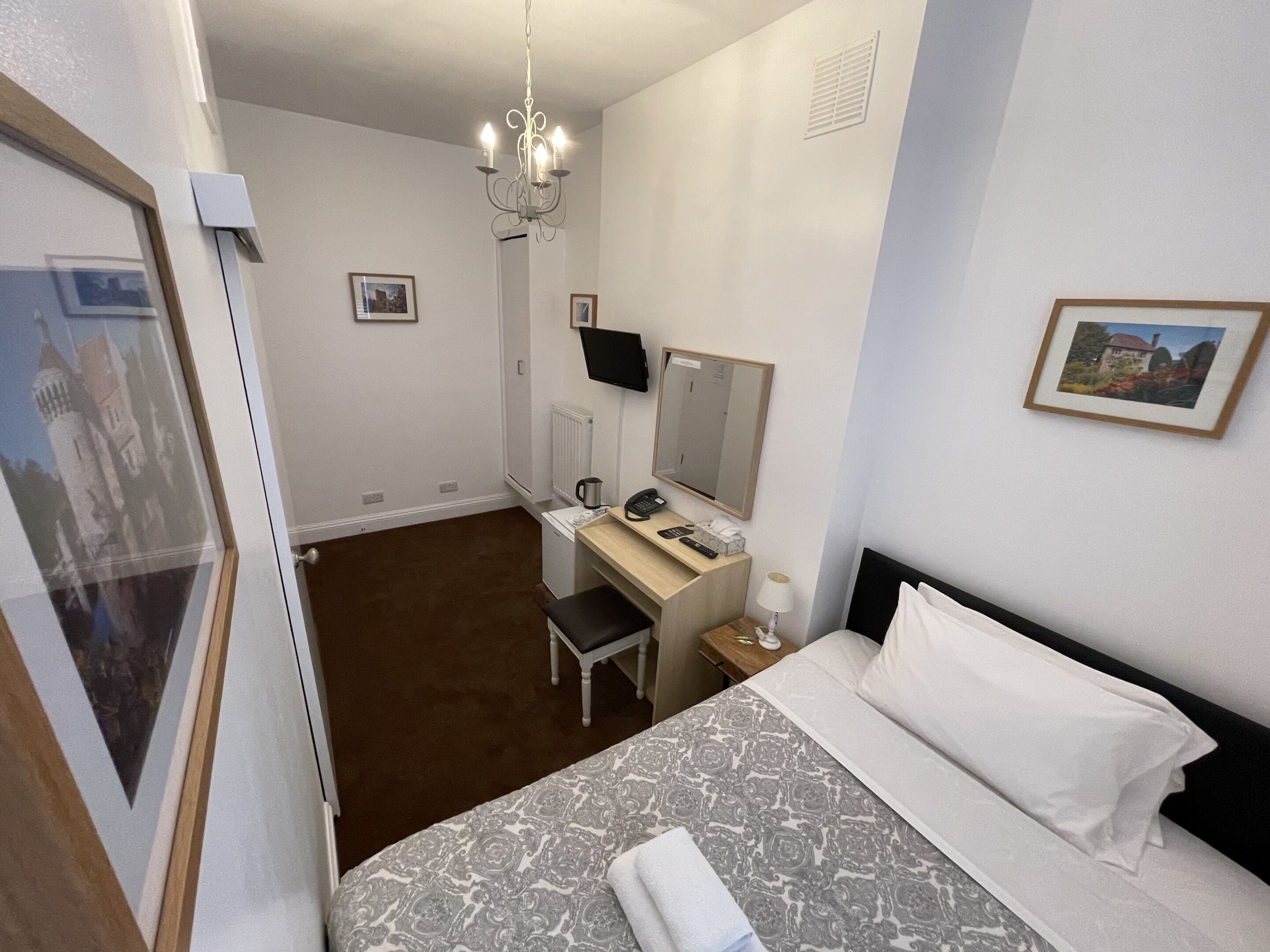 Et hotelværelse med en seng, et skrivebord, en stol, et lille bord med lampe, en telefon og et fjernsyn.