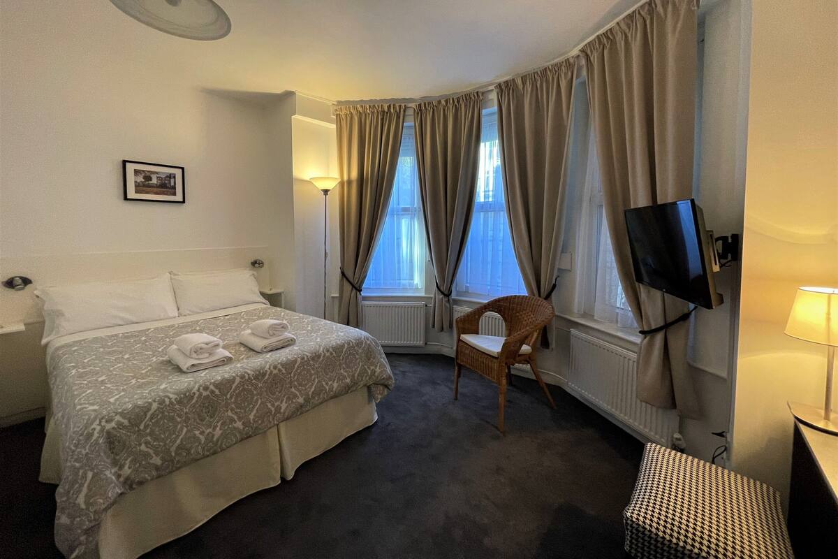 Quarto de hotel com cama, cadeira, televisão e um quadro na parede.
