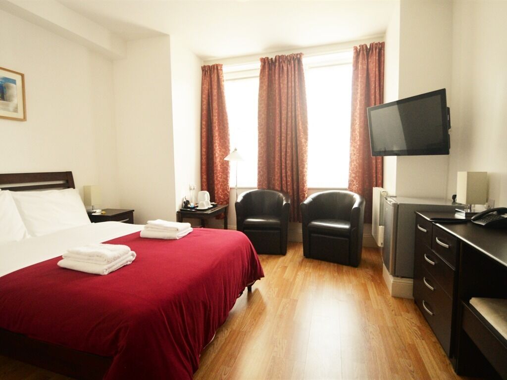 A hotel room with a bed, a desk, two chairs, a TV, and a window with curtains.
