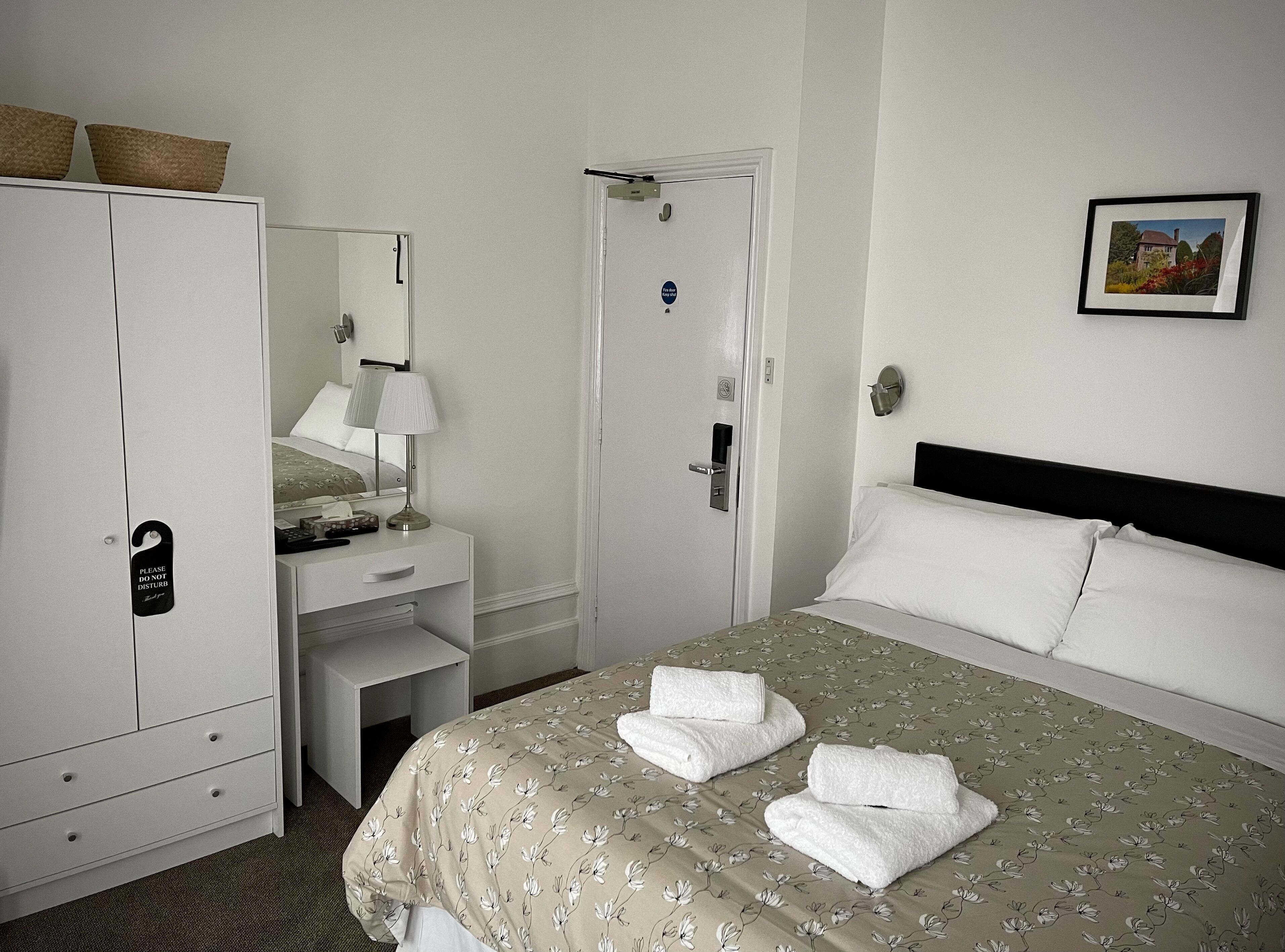 A hotel room with a bed, a desk, a wardrobe, a mirror, and a door.
