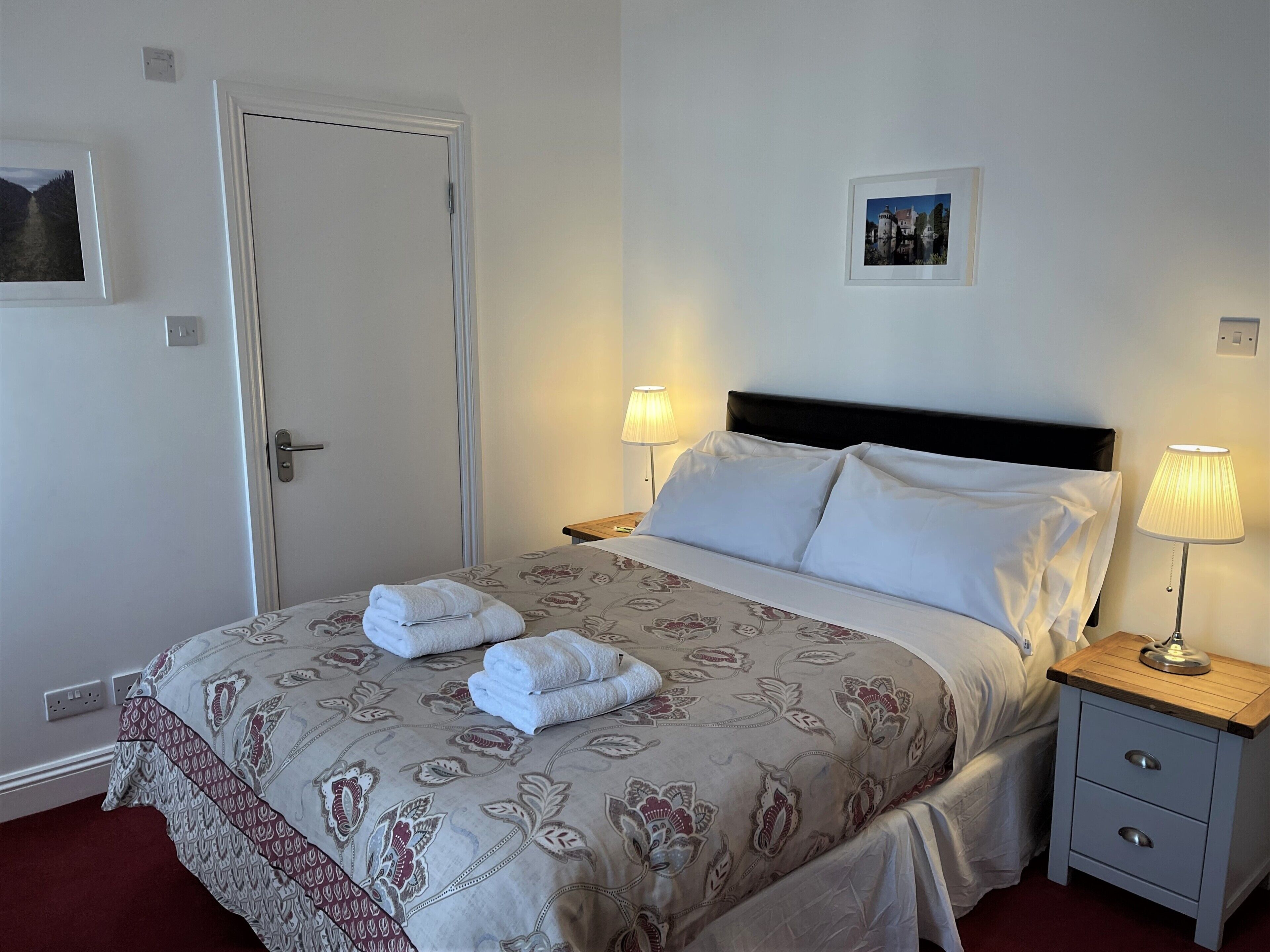 A neatly made bed with a floral-patterned bedspread, two bedside lamps, and a small bedside table with a lamp.